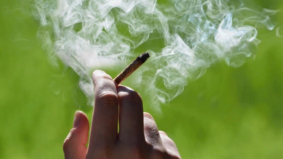 Image of hand holding a lit joint with smoke emitting